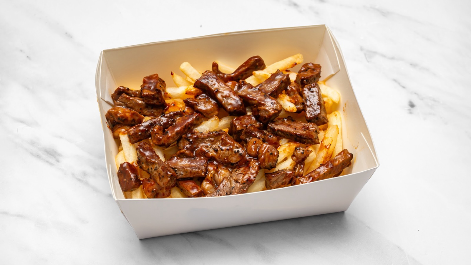 Prime & Crisp Signature Garlic Peppercorn steak strips glazed and piled over chips in a takeaway box